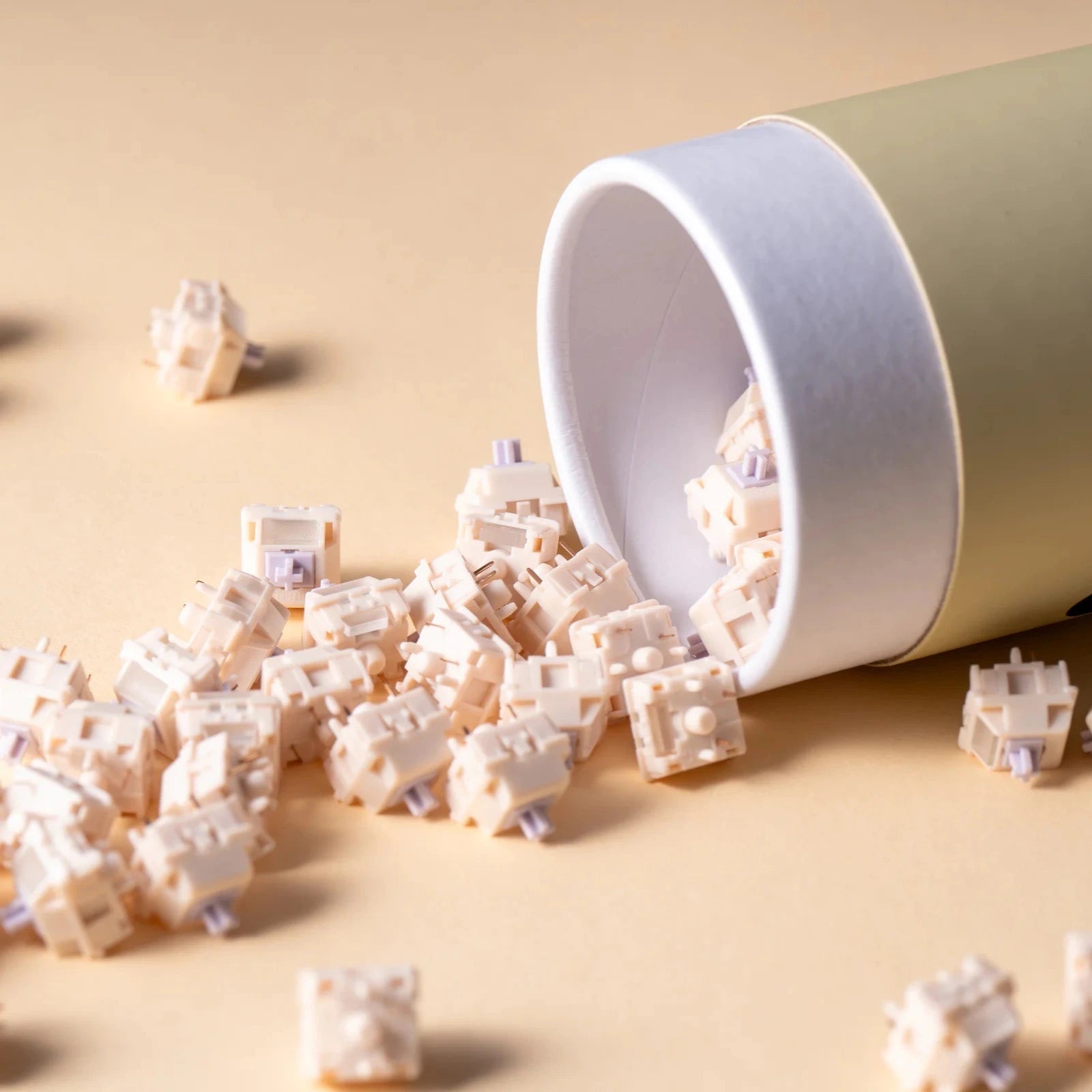 White container with keyboard switches spilling out on a beige background