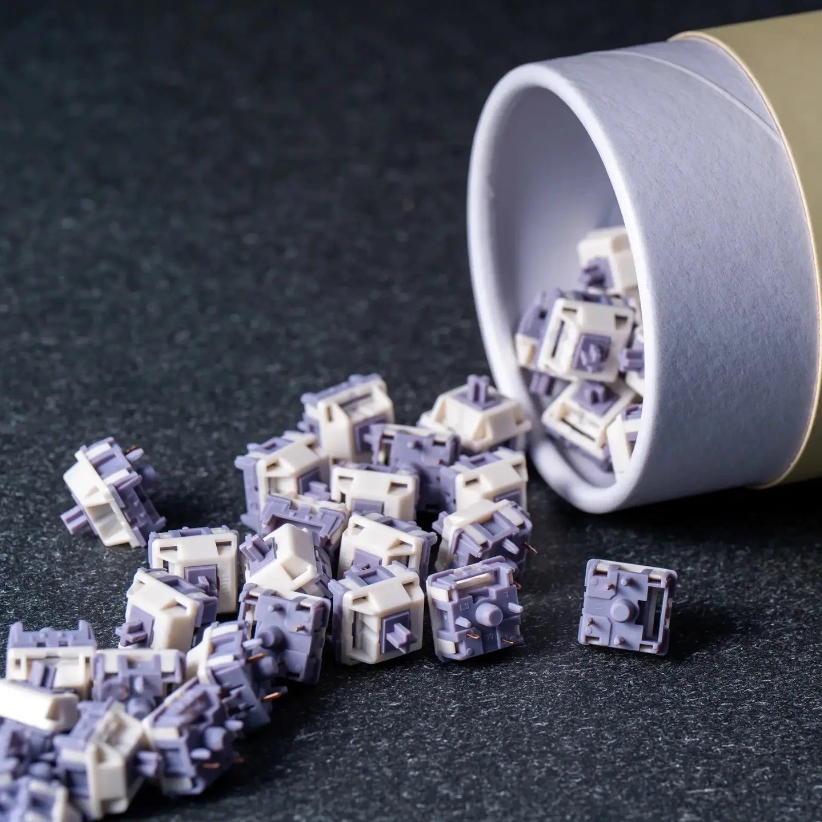 Mechanical keyboard switches spilling out of a white container on a dark surface